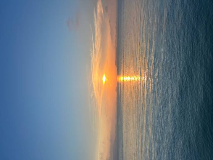 A brilliant orange sun sets over calm ocean waters, its reflection glowing along the gentle ripples.