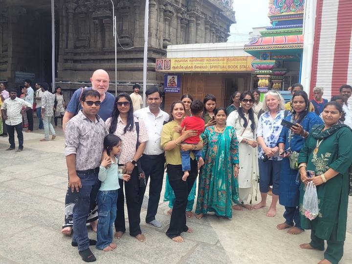 A large mixed group of visitors stands outside a busy South Indian temple entrance and book stall.