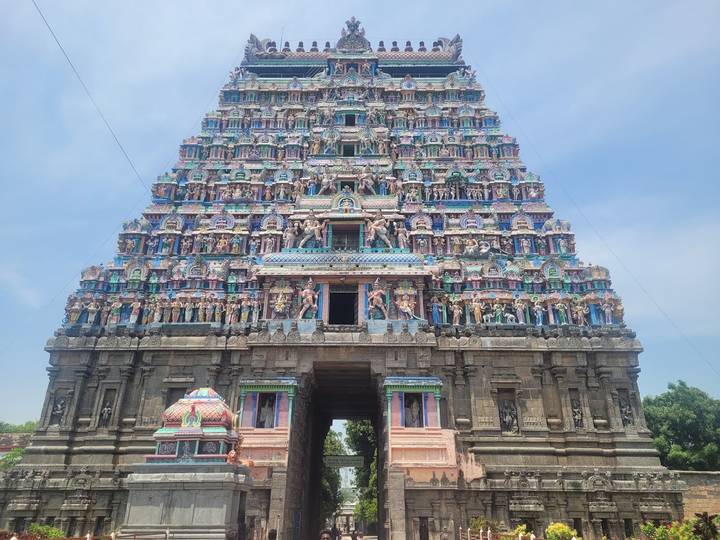 An intricately painted multicolour gopuram tower of a South Indian temple soars into the blue sky.
