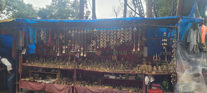 Outdoor stall displaying numerous brass souvenirs and trinkets under a blue tarpaulin.