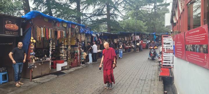 Pedestrian market street lined with souvenir stalls; a monk in red robes walks in the foreground.