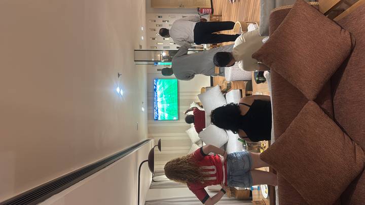 People in a lounge watching a football match on a large TV, drinks on the table.