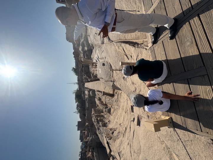 Visitors seated near the unfinished obelisk quarry in bright sunlight while guide explains.