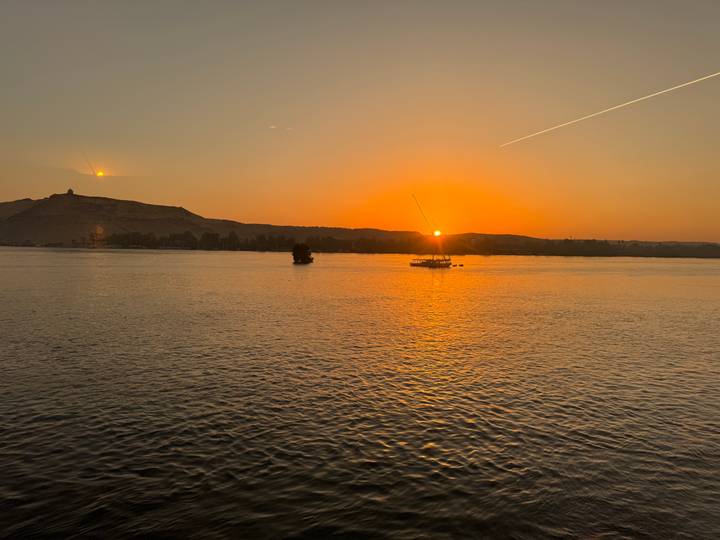 Orange sunset over the Nile with felucca sailboats and a silhouetted hill on the horizon.