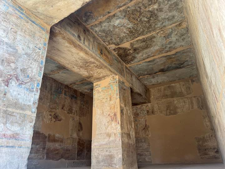 Interior chamber with painted pillars and aged ceiling frescoes of an ancient Egyptian tomb.