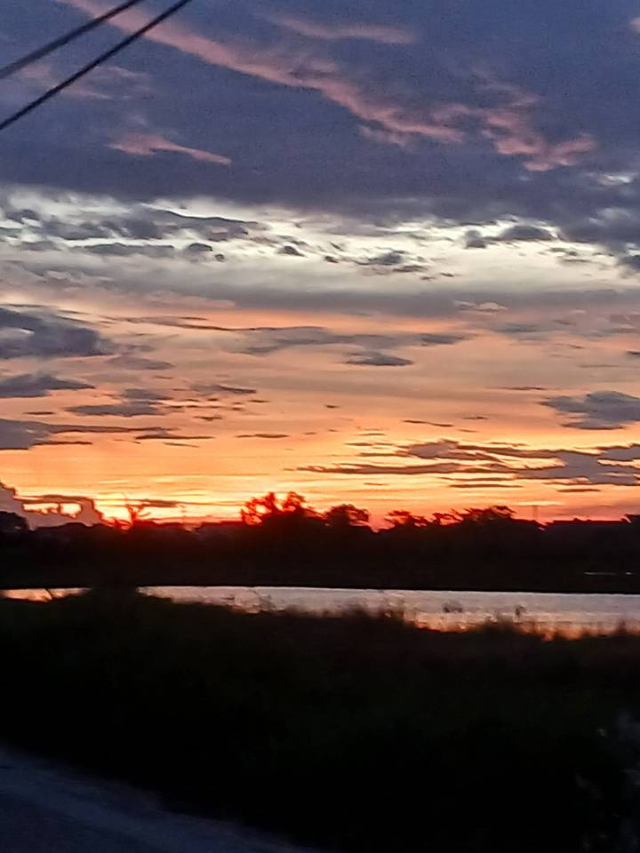 Blurry image of an orange and pink sunset over water with dark cloud formations.