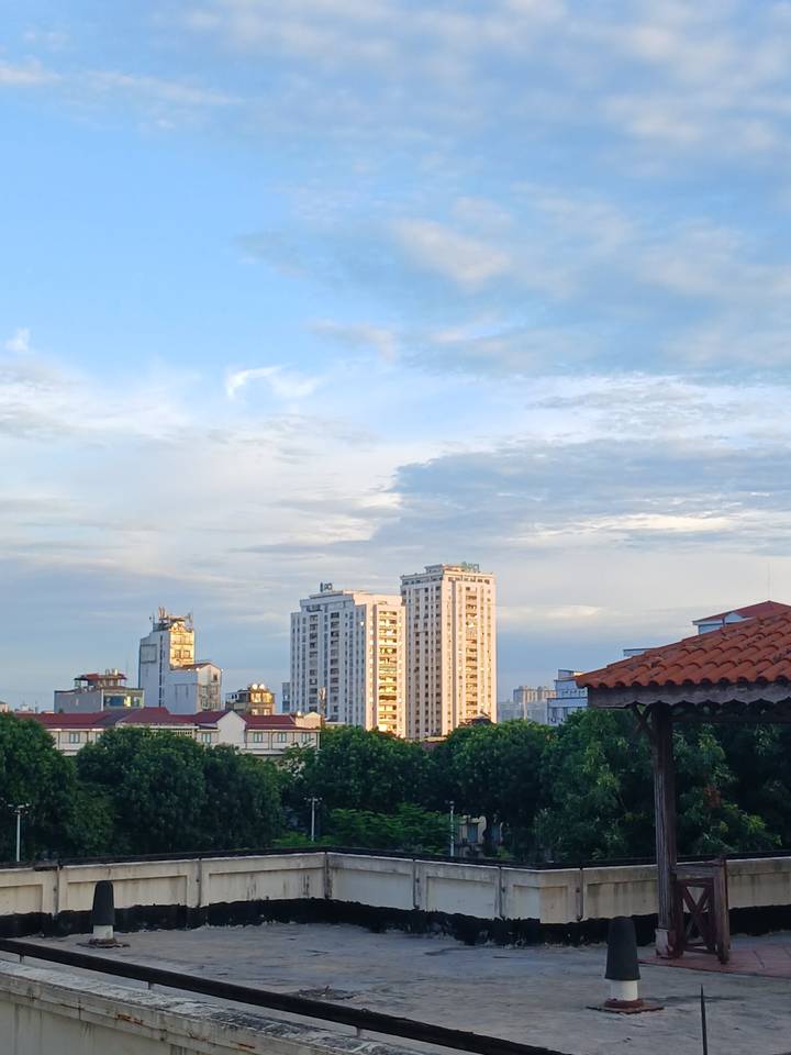 Modern high-rise apartment towers catch warm morning light above a low city skyline and tiled rooftops.