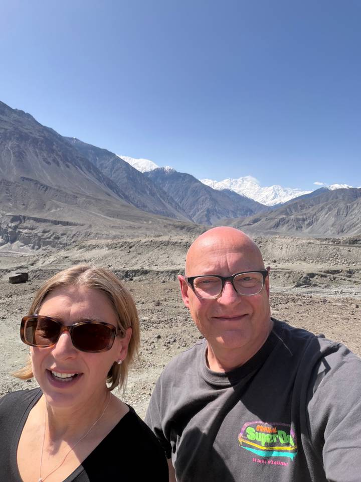 Selfie of two travellers with barren mountain landscape and snowy peaks behind them