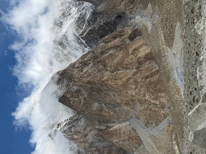 Tall rugged mountain face dusted with snow and shrouded in drifting clouds against blue sky