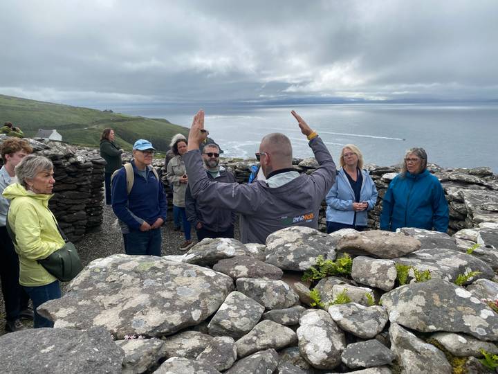 Guide addresses visitors among ancient stone ring fort walls overlooking the Atlantic on a misty day.