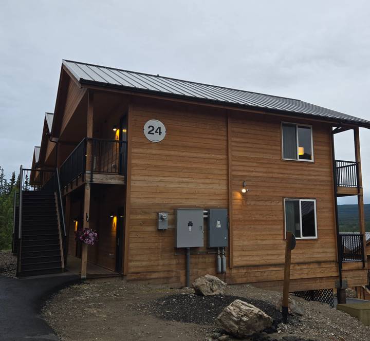 Simple two-story wooden lodge building numbered 24 under grey Alaskan sky.