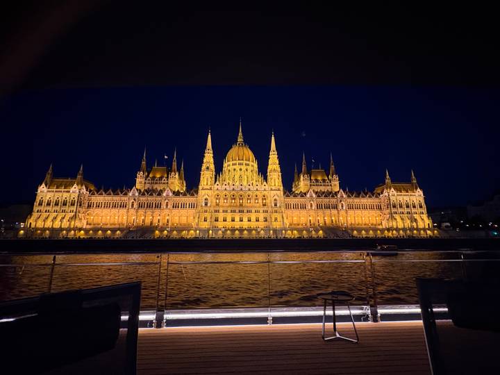 Illuminated Hungarian Parliament Building glowing over the Danube River at night, viewed from a boat deck.