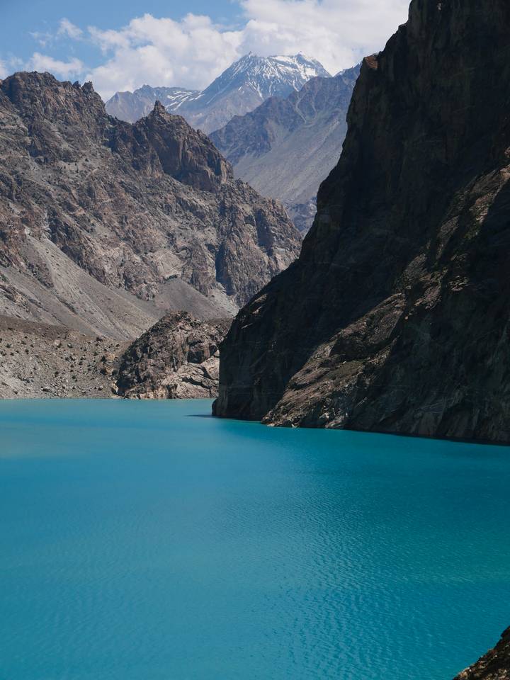 Turquoise mountain lake bordered by steep rocky cliffs in high-altitude Pakistan.