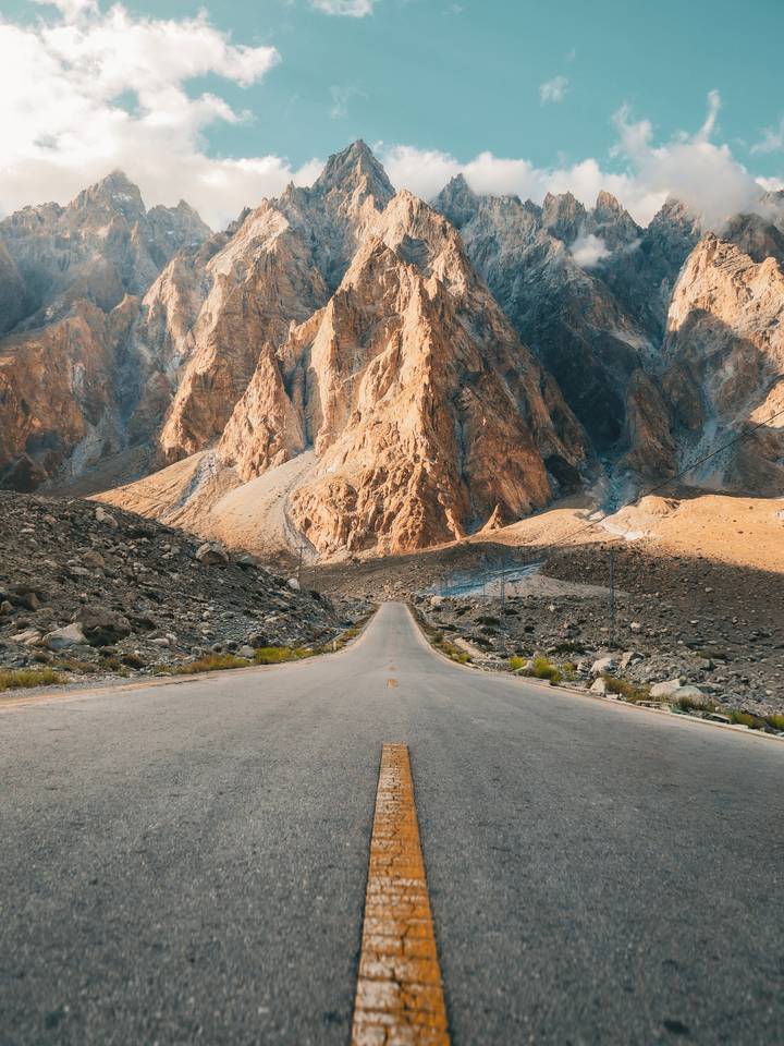 Straight mountain road leading toward dramatic golden peaks on the Karakoram Highway.