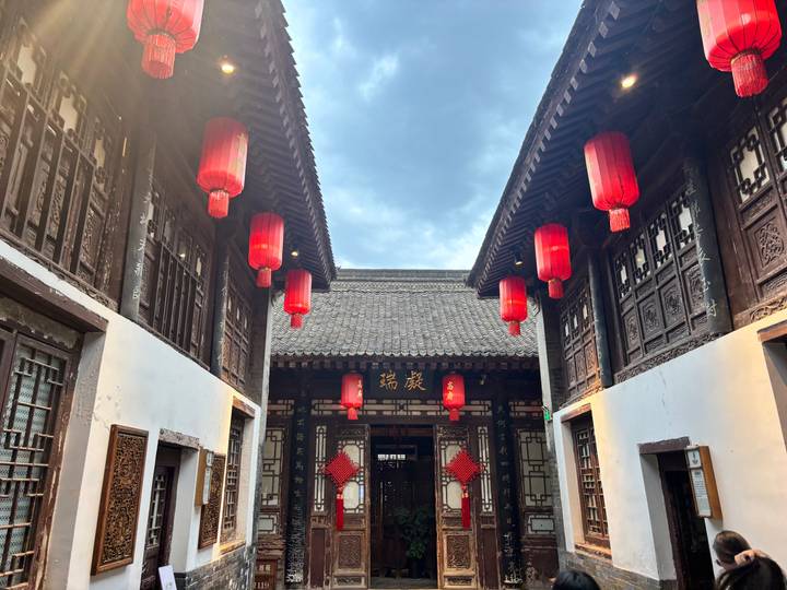 Traditional courtyard with ornate wooden architecture and red lanterns glowing at dusk.