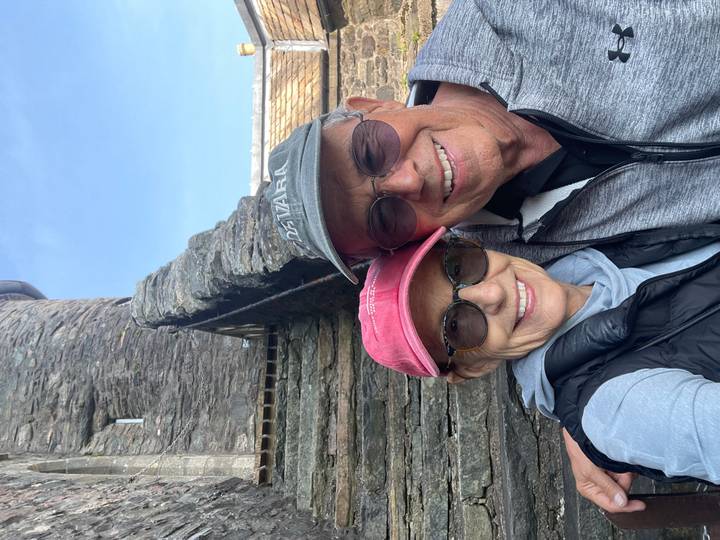 Older couple take a cheerful selfie in front of a stone castle wall under blue skies.
