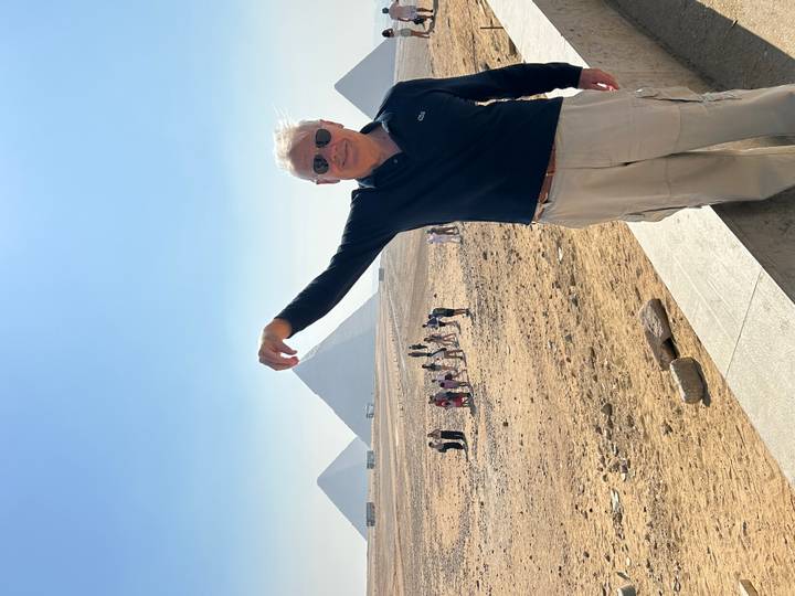 Man playfully pretends to pinch the distant pyramids on a bright desert morning.