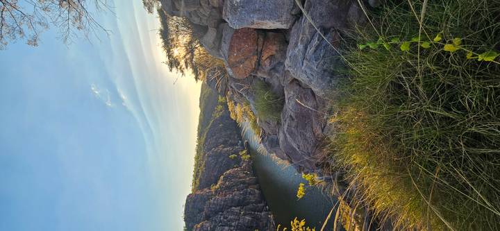 Rocky gorge framed by cliffs and vegetation with a tranquil river flowing below under warm afternoon light
