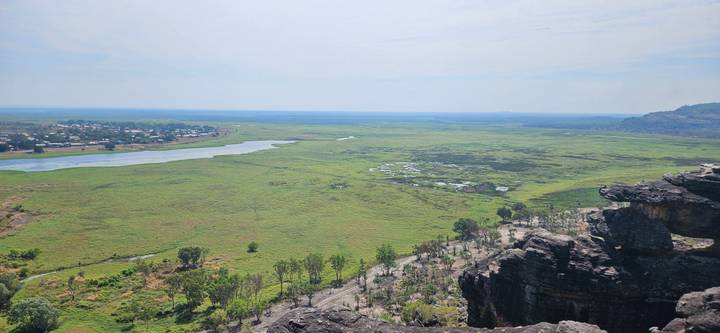 Expansive green wetland plain viewed from a rocky escarpment with distant village and river