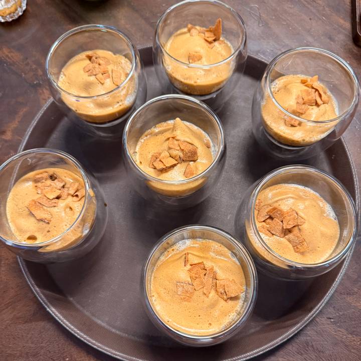 Close-up overhead view of several double-walled glasses filled with creamy Vietnamese egg coffee topped with crunchy flakes.
