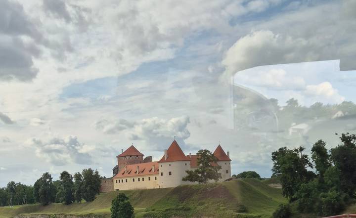 Stone castle on hill photographed through bus window with reflections.