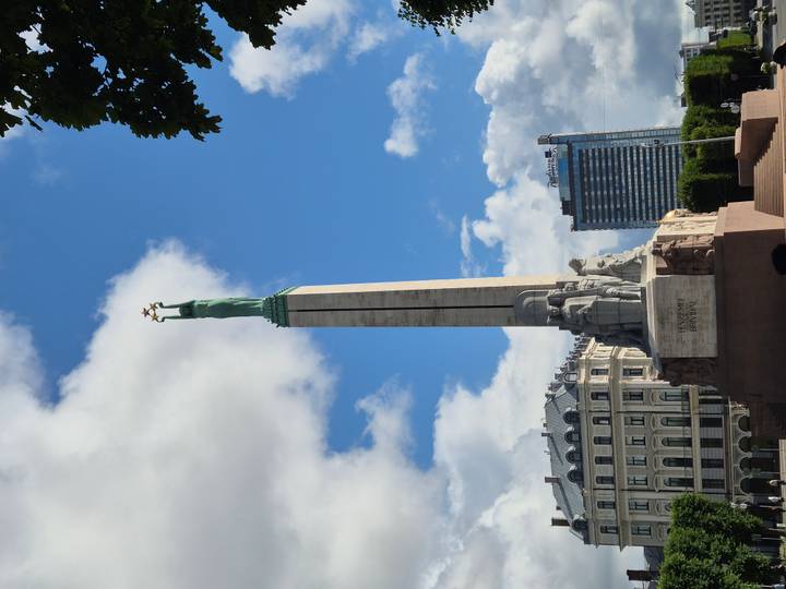 Freedom Monument towers above Riga cityscape under bright blue sky.