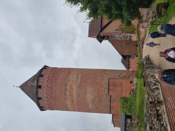 Brick tower and medieval walls of Turaida Castle with tourists walking.