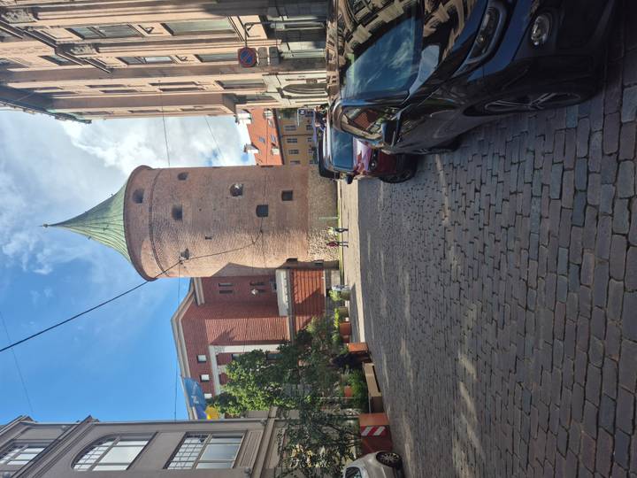 Powder Tower rises above cobblestone street lined with parked cars in Riga.