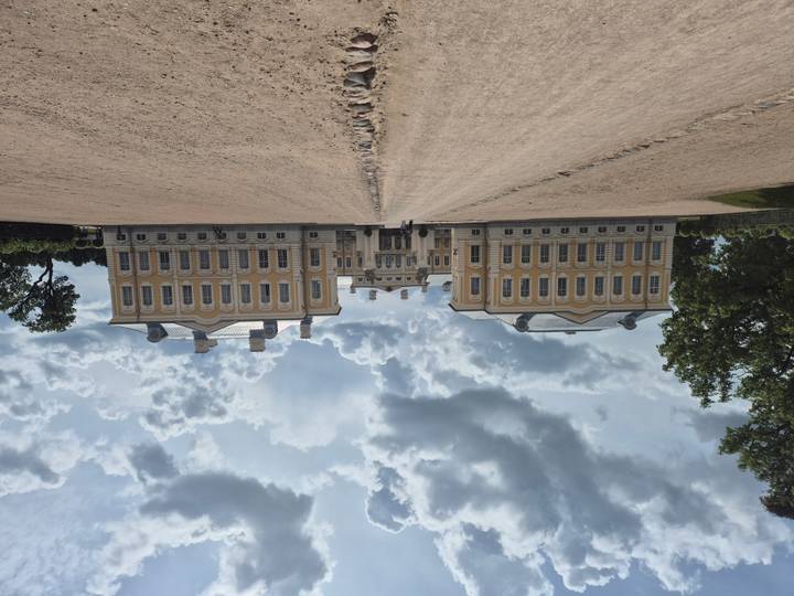 Grand Rundale Palace under dramatic clouds viewed from long sandy avenue.