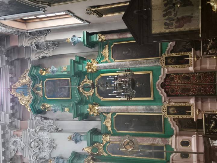 Green and gold baroque altar with chandeliers inside ornate church.