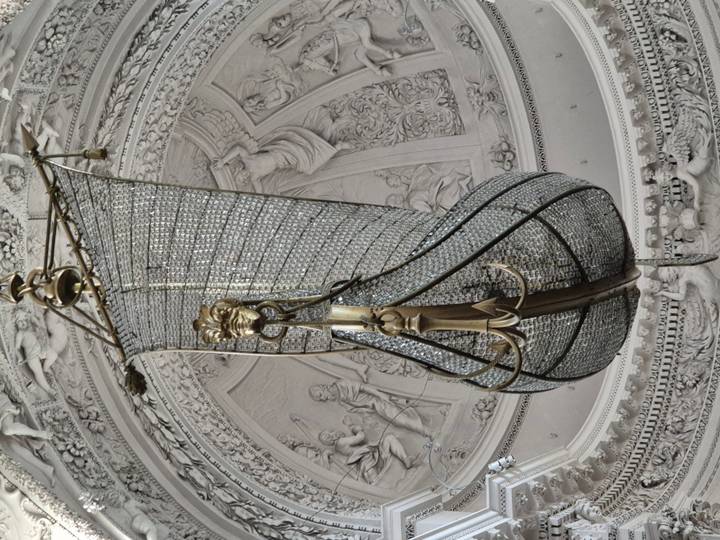 Intricate ship-shaped crystal chandelier hanging from ornate church ceiling.