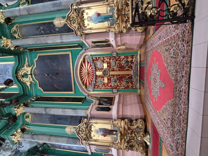 Colourful Orthodox iconostasis with ornate cross and carpets.