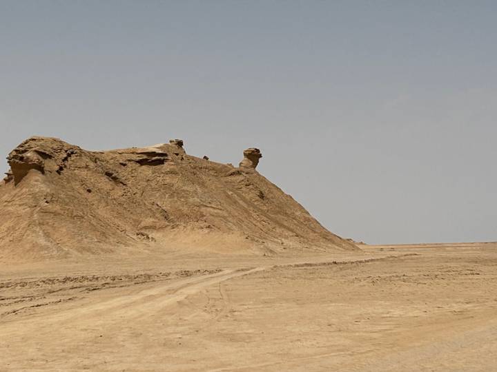 Isolated wind-carved sandstone outcrop and barren desert plain beneath a pale hazy sky in southern Tunisia.