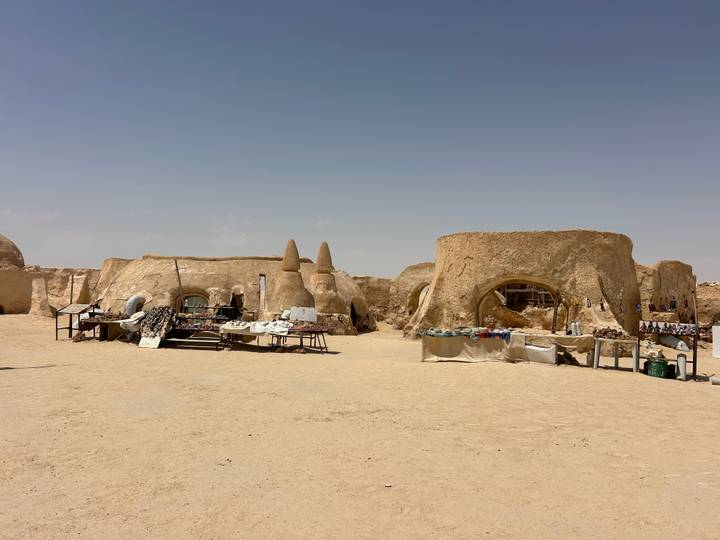 Earth-colored circular huts and market tables of the Star Wars Mos Espa film set stand in the open desert.