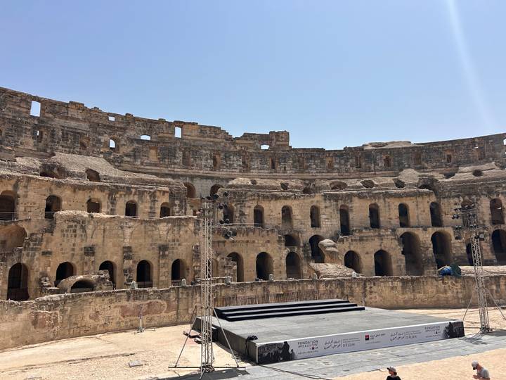 Interior stone arches and tiered seating of the ancient Roman amphitheatre at El Jem lit by midday sun.