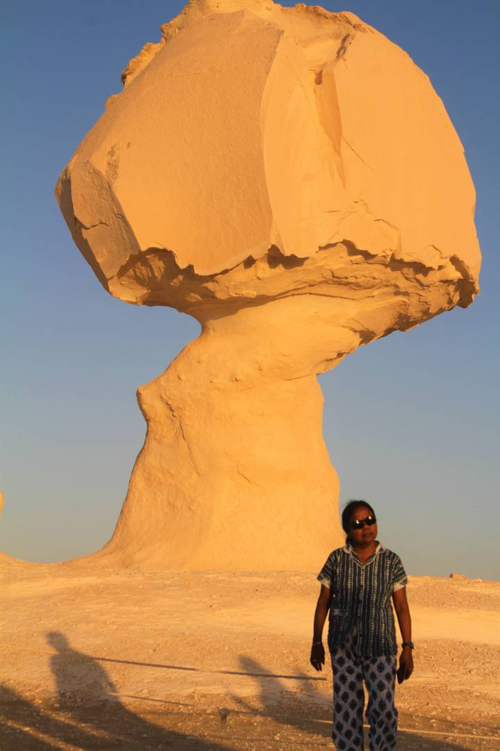 Traveler standing beside a towering mushroom-shaped chalk formation glowing in the desert sunset.