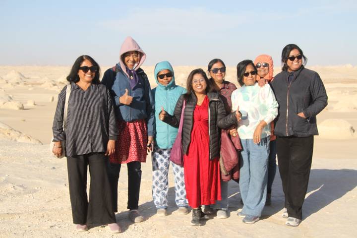 Group of smiling women giving thumbs up in the sandy expanse of Egypt's White Desert.