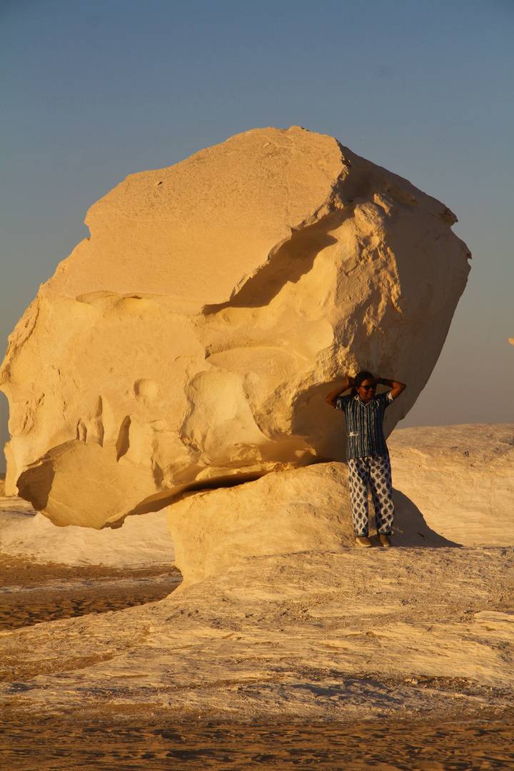 Traveler relaxing against a sculpted white rock under warm evening light in Egypt’s White Desert.