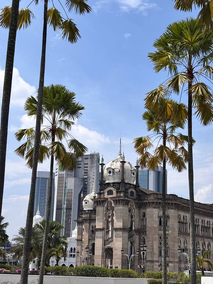 Colonial dome building framed by tall palm trees against bright blue sky in Kuala Lumpur