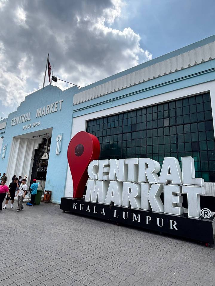 Entrance of Kuala Lumpur's Central Market with large Google-pin sculpture and people walking in front of the pale-blue art-deco façade.