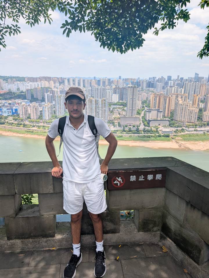 Traveller poses on an overlook with expansive urban skyline and river far below.