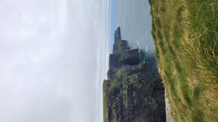 Dramatic sheer cliffs plunge into the Atlantic Ocean under a grey sky at the Cliffs of Moher.