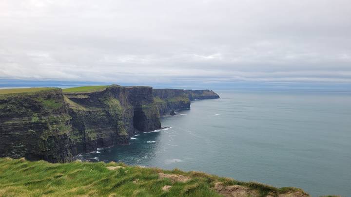 Wide panorama of the Cliffs of Moher stretching across the horizon above calm grey sea.