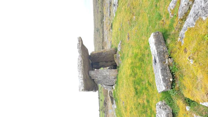 Ancient stone dolmen standing on a grassy limestone plain under a bright white sky.