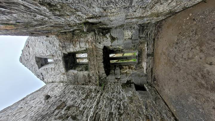 Rugged interior walls and window openings of a stone medieval ruin viewed from ground level.