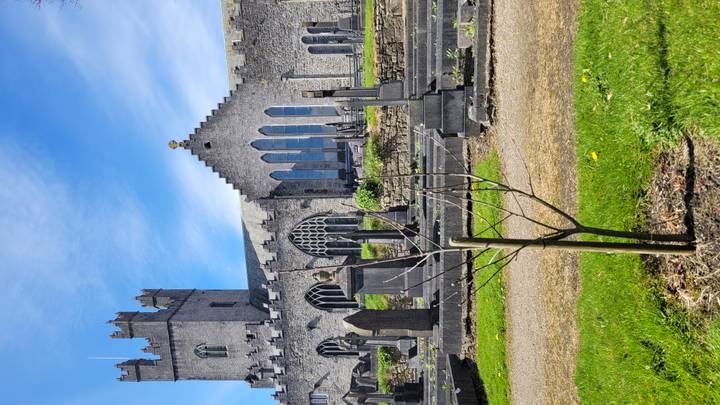 Gothic stone church with tall windows and adjoining graveyard under a clear blue sky.