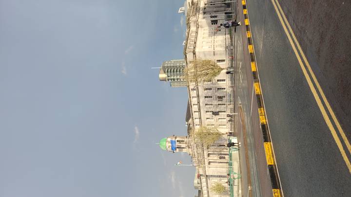 Neoclassical Custom House with green dome along riverside road after rainfall, rainbow light on facade.