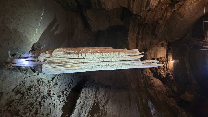 Massive illuminated stalactite hanging in a dimly lit limestone cave chamber.