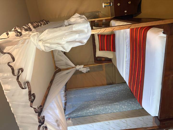 Interior of a safari camp bedroom with single canopy bed dressed in white and red fabrics.