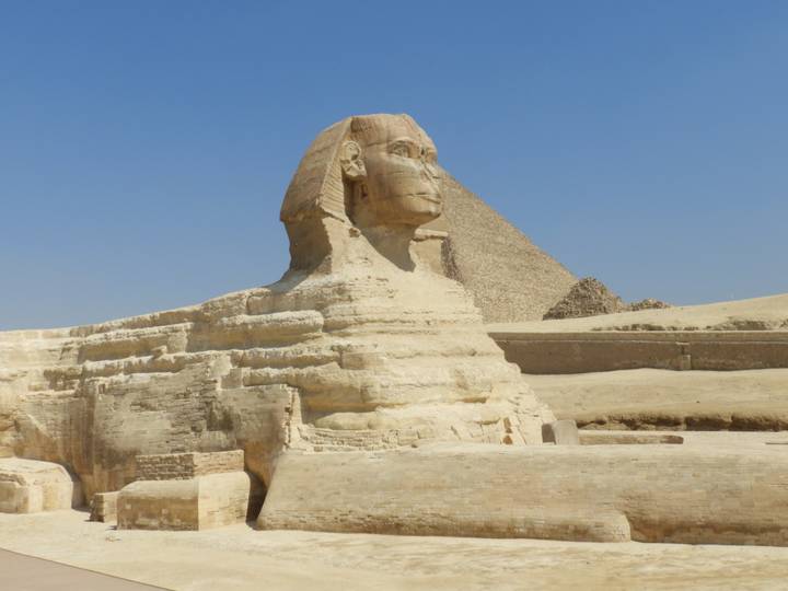 Great Sphinx of Giza with pyramid backdrop under cloudless blue sky
